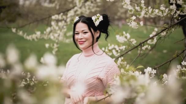 Очаровательная азиатская брюнетка позирует в цветущем фруктовом саду — стоковое видео
