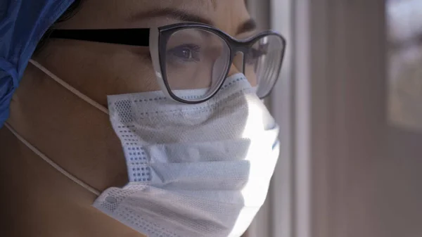 Серьёзная женщина в маске и очках, смотрящая в окно — стоковое фото
