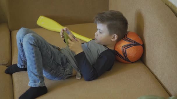 Borred kleine jongen spelen van games op de smartphone leggen op een sofe en bal. — Stockvideo