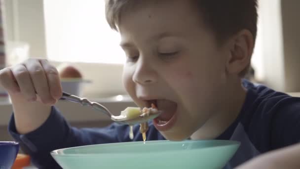 Jonge jongen eet soep zittend aan eettafel — Stockvideo