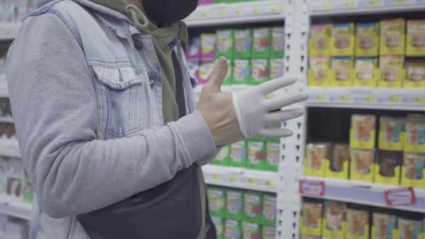 Mężczyzna w masce stoi w centrum handlowym i zakłada gumowe rękawiczki.. — Wideo stockowe