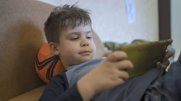 Niño juega en el teléfono móvil acostado en el sofá — Foto de Stock