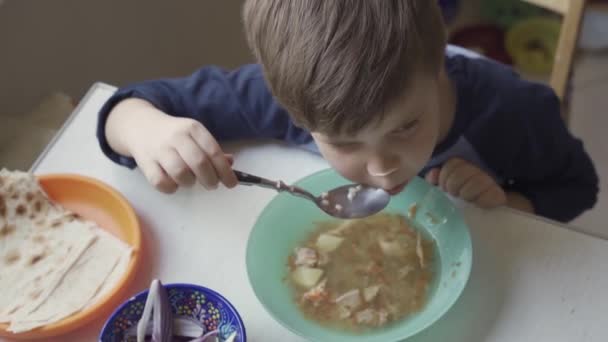 Niño pequeño comiendo sopa sentado a la mesa solo — Vídeo de stock