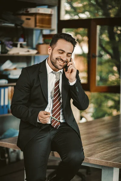 Alegre feliz hombre de negocios habla con el teléfono móvil sentado en el escritorio —  Fotos de Stock