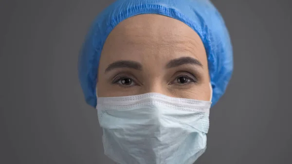 Feminino Médico em máscara protetora e tampa azul, close-up rosto isolado na parte traseira cinza — Fotografia de Stock
