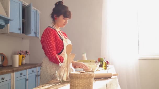 Egy fiatal lány főz egy vintage konyhában próbál emlékezni az összetevőkre. Megujjazza a lisztet, ami egy felhővel fejlődik az ablak hátterében. Oldalnézetből. Gyümölcsfélék — Stock videók