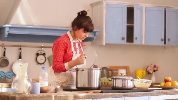 Dziewczyna gotuje w pięknej kuchni, otwierając garnek wrzącej wody lub zupy, sól danie i szczęśliwie zamyka garnek. Dziewczyna gotuje w zabytkowej lub staromodnej niebieskiej kuchni. Prores 422 — Wideo stockowe