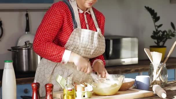 Lány pék gyúrja a tésztát áll a régi divat konyha egy piros ruhát. Egy pék tésztát gyúr, hogy kenyeret vagy tekercset csináljon a konyhában. Gyümölcsfélék — Stock videók