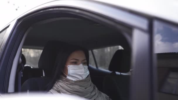 Pensando em algo de etnia asiática, uma mulher com uma máscara protetora senta-se em um carro com direção pela direita e olha para o lado. Prores 422 — Vídeo de Stock