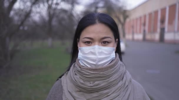 보호용 마스크를 쓴 아시아 계 여성이 버려진 오래 된 공장 근처의 거리에 서 있습니다. 카메라가 일반 계획으로 떠나는 모습을 가까이 서 찍고 있습니다. 프로방스 422 — 비디오