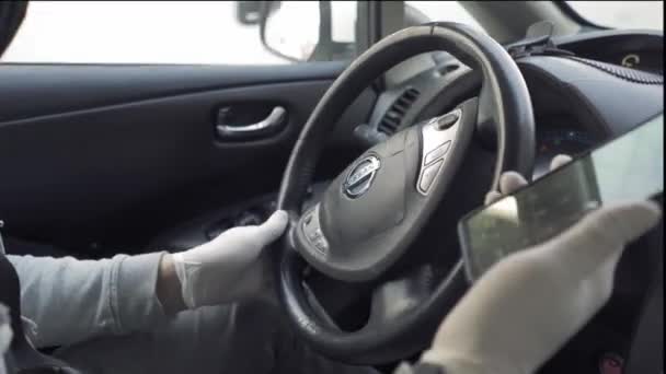 Un conducteur masculin dans une voiture Nissan écrit un message sur un téléphone intelligent pendant qu'il conduit une voiture. Le conducteur conduit une voiture avec des gants jetables pendant la pandémie de coronavirus. Prores 422. Kiev, Ukraine. Avril 2020 — Video