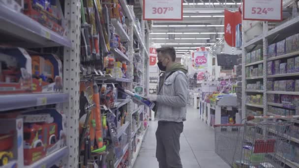 Hombre en una tienda vacía o centro comercial eligiendo juguetes para un niño que se queda en casa en cuarentena. Hombre comprador durante la pandemia de coronavirus. Prores 422. Auchan, Kiev, Ucrania. abril 2020 — Vídeos de Stock