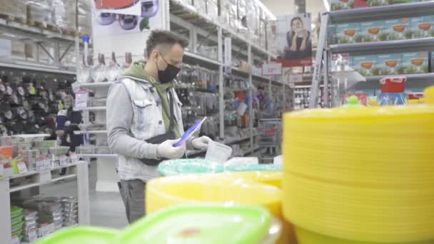 De man met het masker op zijn gezicht selecteert de goederen in de winkel terwijl hij lunchdozen bekijkt. Winkelen tijdens de coronavirus pandemie. Prores 422. Auchan, Kiev, Oekraïne. april 2020 — Stockvideo