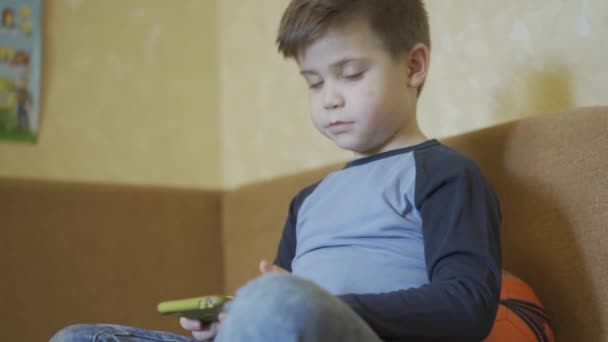Kisfiú beszél a szülők a kamera mögött, miközben játszik online játékok vagy oktatási játékok okostelefon ül a kanapén labda mögött. Maradj otthon koncepciónál. Gyümölcsfélék — Stock videók