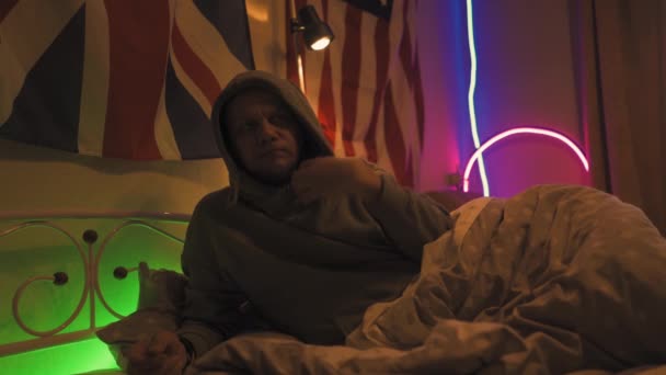 Ο άνθρωπος παίζει στο τάμπλετ ενώ ξαπλώνει στο κρεβάτι ντυμένος με κουκούλα, το βάζει στην άκρη και παίρνει θερμόμετρο κάτω από το χέρι του, το κοιτάζει αναστατωμένο από την υψηλή θερμοκρασία του σώματός του. Σχέδιο καραντίνας. Πρότυπα 422 — Αρχείο Βίντεο