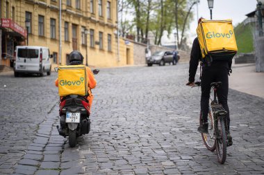 Two Glovo delivery men competition with Yellow Glovo backpacks on bike and on motobike. Glovo food delivery service concept. Kyiv, Ukraine, 24th of April 2020, Andreevskiy spusk Street clipart
