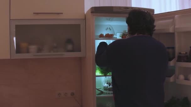 Der Ehemann ist unterernährt und öffnet den Kühlschrank, nimmt Würstchen und isst roh in dem Moment, als die Frau das Licht einschaltet. Übergewichtige. Bleiben Sie zu Hause. Prores 422 — Stockvideo