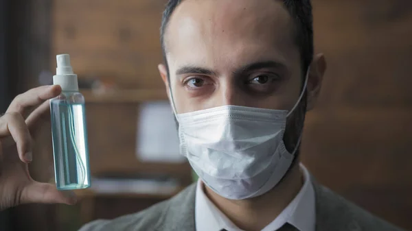 Omul cu mască de protecție demonstrează sticla de lichid antiseptic pentru tratarea mâinilor și a suprafețelor de lucru pentru a preveni infecția cu virusul. Închideți portretul unui om de utilitate care deține spray de dezinfectant — Fotografie, imagine de stoc