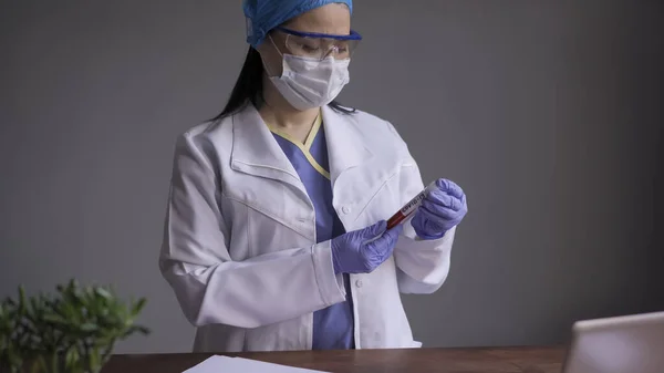 Medicul examinează tubul sanguin al bolnavilor de coronavirus sau covid 19 în biroul de laborator. Femeie lucrător medical purtând uniformă de protecție medicală — Fotografie, imagine de stoc