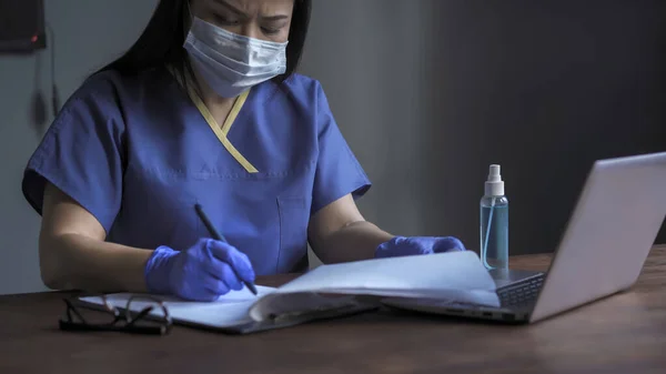 Médico mujer cansada llena formularios médicos, Mujer escribe con un bolígrafo en papel sentado en el escritorio mientras trabaja en la computadora en su oficina — Foto de Stock