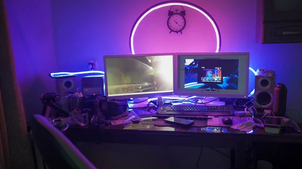 Modern work place of creative man or freelancer. Table with computer and digital gadgets on it in home interior with neon glows