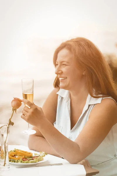 Glückliche Frau lächelt und hebt ein Glas Wein oder Champagner vor dem Hintergrund des Sandstrandes. Festlicher Toast zu Ehren eines denkwürdigen Ereignisses oder Hochzeitstages. Getöntes Bild — Stockfoto