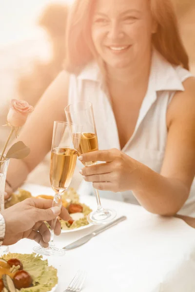 Glad kvinna ler med ett glas vitt vin. Mogna par har event utomhus på strandcaféet. Selektivt fokus på människohänder med glas vin eller champagne i förgrunden. Tonad bild — Stockfoto
