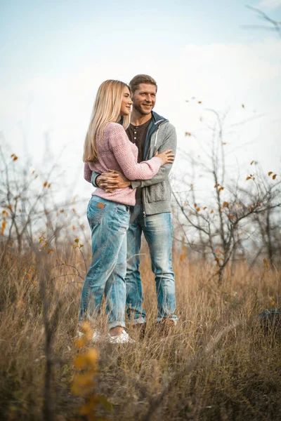 Abraçando casal sorrindo em pé na grama de outono ao ar livre, jovens abraçando na natureza contra um céu azul — Fotografia de Stock