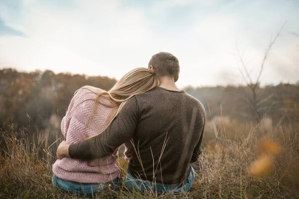 Rückansicht umarmender Touristen, die auf der Klippe sitzen und den Duft der herbstlichen Natur im Freien einatmen — Stockfoto