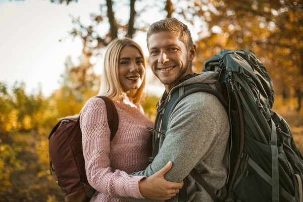 Heureux routards amoureux rit câlins tout en regardant la caméra et debout dans le contexte de la nature d'automne — Photo