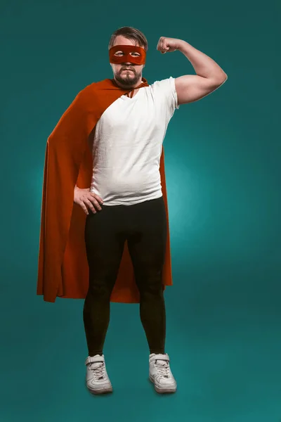 Super Hero Man pokazuje swoje mięśnie i gotowy uratować świat. Poważny człowiek w czerwonym super masce bohatera i płaszcz pokazuje swoje mięśnie patrząc przed kamerą. Wytnij na zieleni Biscay tle — Zdjęcie stockowe
