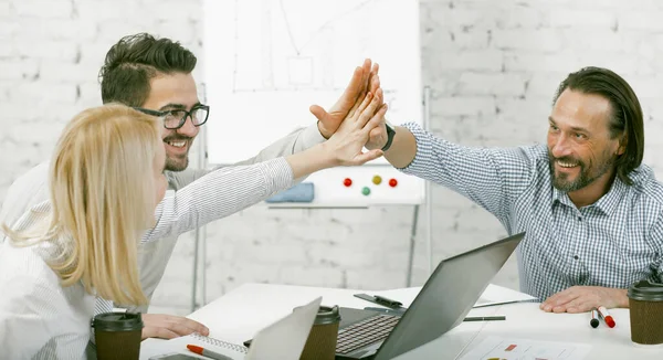 Un gesto de choca esos cinco. Colegas unieron sus manos en señal de unidad sentadas en el escritorio. Los empresarios felices se regocijan por un proyecto exitoso. Trabajo en equipo del equipo empresarial en la oficina — Foto de Stock