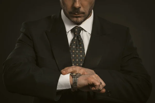 Businessman checking time on his wrist watch. Close up portrait of business man looking at clock on hand. Front view of serious bearded man in black suit — Stock Photo, Image