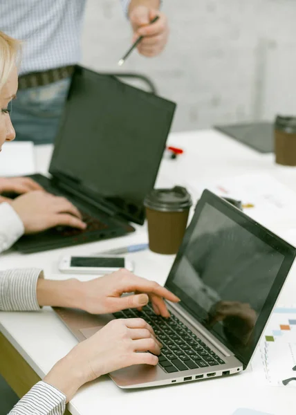 Close-up hands of office workers typing on laptop. Team work on new project. People uses computer and drinks coffee while sitting at table together. Coworking of business people in office — Stock Photo, Image