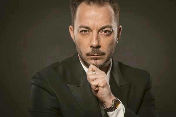 Serious Businessman touches the chin on grey background. Portrait of a successful confidence man in elegant formalwear looking at the camera. — Stock Photo, Image