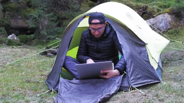 Freelancer or businessman sitting in a tent on nature doing business using a laptop and cellular connection to Internet. Self-isolation during quarantine. Carpathian Mountains, Ukraine. Prores 422 — Stock Video