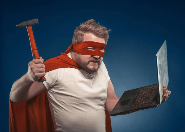 Superhrdina muž drží notebook v jedné ruce a kladivo v druhé ruce — Stock fotografie