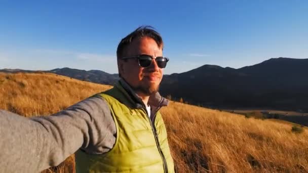 Блог подорожей знімає історію на вершинах гір. Молодий чоловік тримає фотоапарат у руці, фотографуючи себе і краєвиди з вершини гір. Карпатські гори, Україна. Проходить 422 — стокове відео