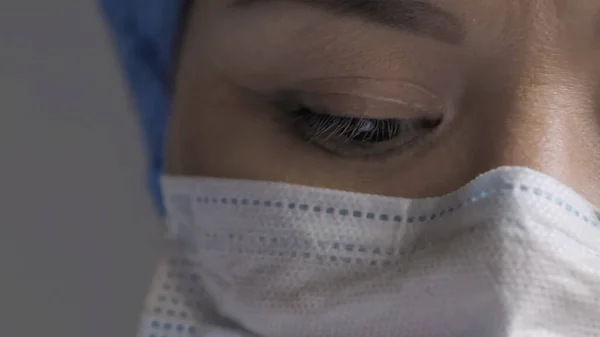 Уставший глаз доктора. Женщина в защитной маске смотрит вниз, молодая женщина истощена от переутомления во время пандемии коронавируса, вблизи женского глаза медика. Копирование пространства слева — стоковое фото