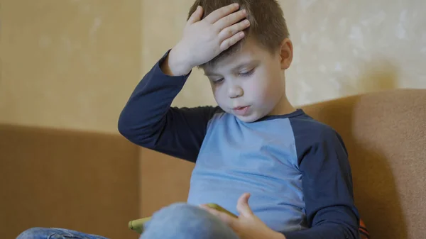 Barn använder mobiltelefon sittandes på soffan hemma. Liten pojke spelar dataspel på sina pappor mobiltelefon medan stanna hemma under ett virusutbrott. Begreppet pandemi — Stockfoto