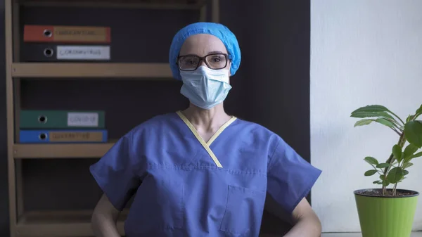 Dokter yang lelah melihat kamera mengenakan seragam medis pelindung, masker, topi dan kacamata. Perawat perempuan merasa stres karena terlalu banyak bekerja selama pandemi — Stok Foto