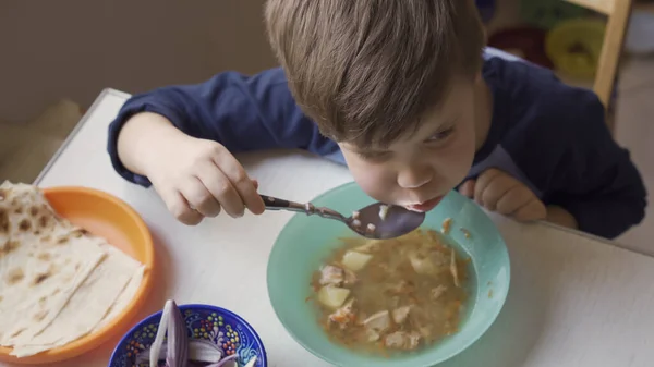 A fiú levest eszik az ebédlőasztalnál, friss hagymával és pitakenyérrel. Magas látószögű — Stock Fotó