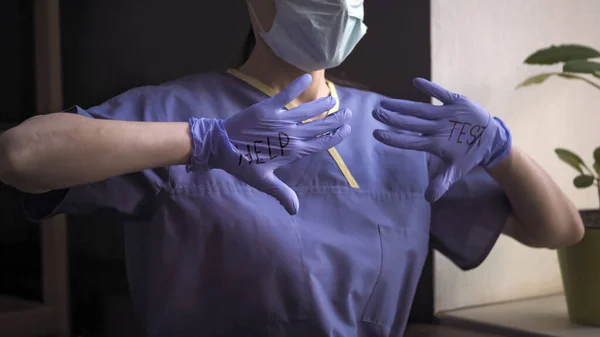 Doctorul arată sloganul Help Test scriind pe palmele deschise purtând mănuși albastre. Medic în uniformă albastră de protecție, Împușcat de aproape — Fotografie, imagine de stoc