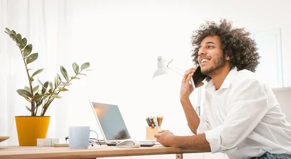 En leende affärsman pratar över telefon. Ung man som förhandlar online på en mobiltelefon när han arbetar hemifrån på ett distansarbete. Arbete hemifrån koncept — Stockfoto