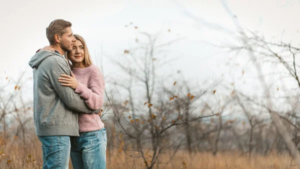 可爱的夫妻在秋天的自然景观的背景下，站在拥抱中休息。年轻的高加索男女拥抱在模糊的年轻森林背景上。右边的复制空间 — 图库照片
