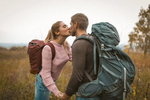 热爱背包的人在户外的田野里亲吻。一对快乐的夫妇,年轻的男男女女站在秋天的大自然的背景下.爱冒险的概念 — 图库照片