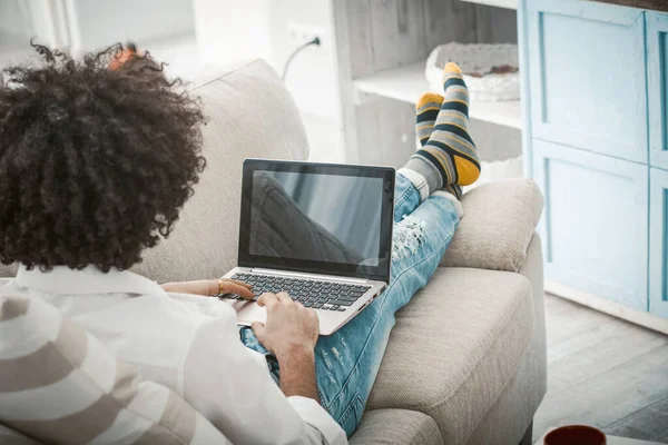 Laptop de trabalho millennial criativo no sofá. Visão traseira do homem deitado no sofá e trabalhando de casa no laptop. Fechar a tela de computadores com espaço em branco preto — Fotografia de Stock