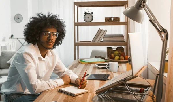 A kreatív ember jegyzetlaptoppal ír a Home Workplace-ben. Arab üzlet, vagy szemüveges diák, aki a kamerába néz. Szabadúszó ötlet. Otthoni munka — Stock Fotó