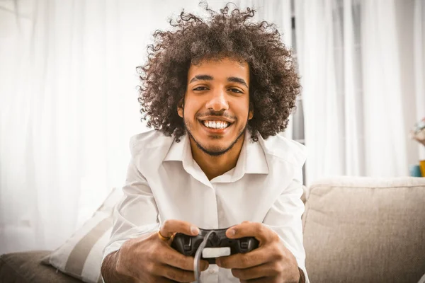 Arabic gay playing computer game. Young man holds Play Station joystick sitting at sofa in backlit. Smiling handsome looking at camera. Funny self-isolation concept — Stock Photo, Image