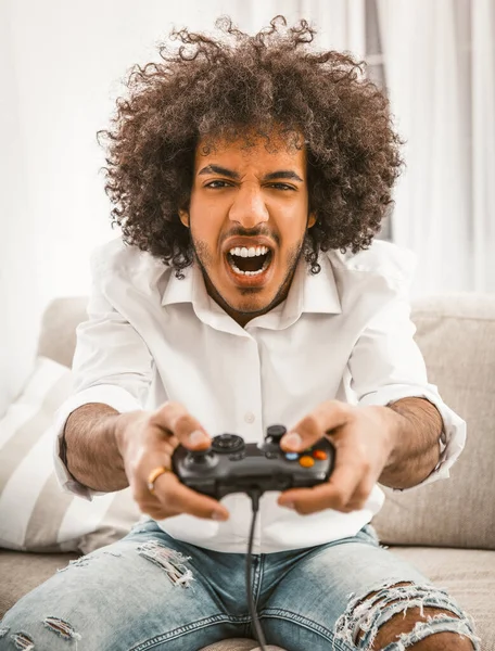 Urlando spara giocatore o attacchi nel gioco per computer. Il concetto di emozioni. Giovane arabo gioco per computer seduto sul divano in casa interna — Foto Stock